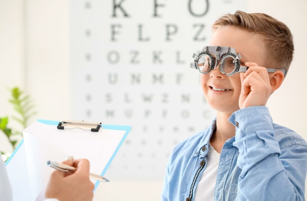 A child smiling while a professional adjusts a pair of metal trial frames during a pediatric eye exam.