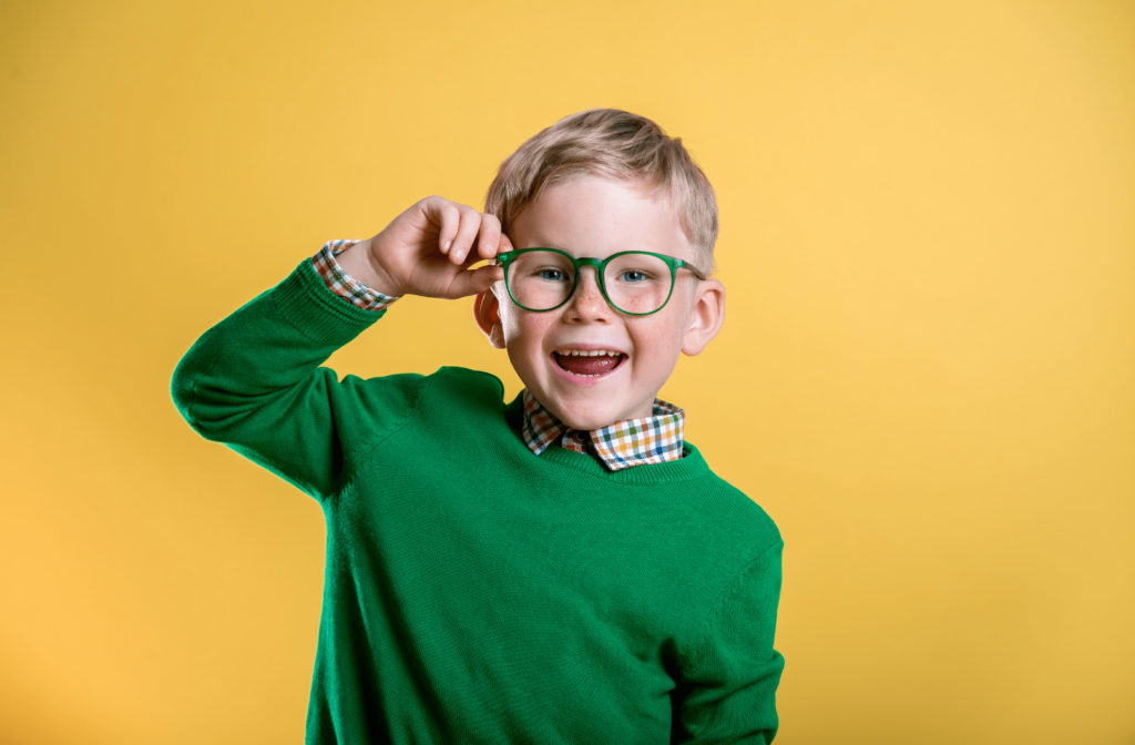 A young boy smiling and wearing a green shirt and green glasses for myopia control