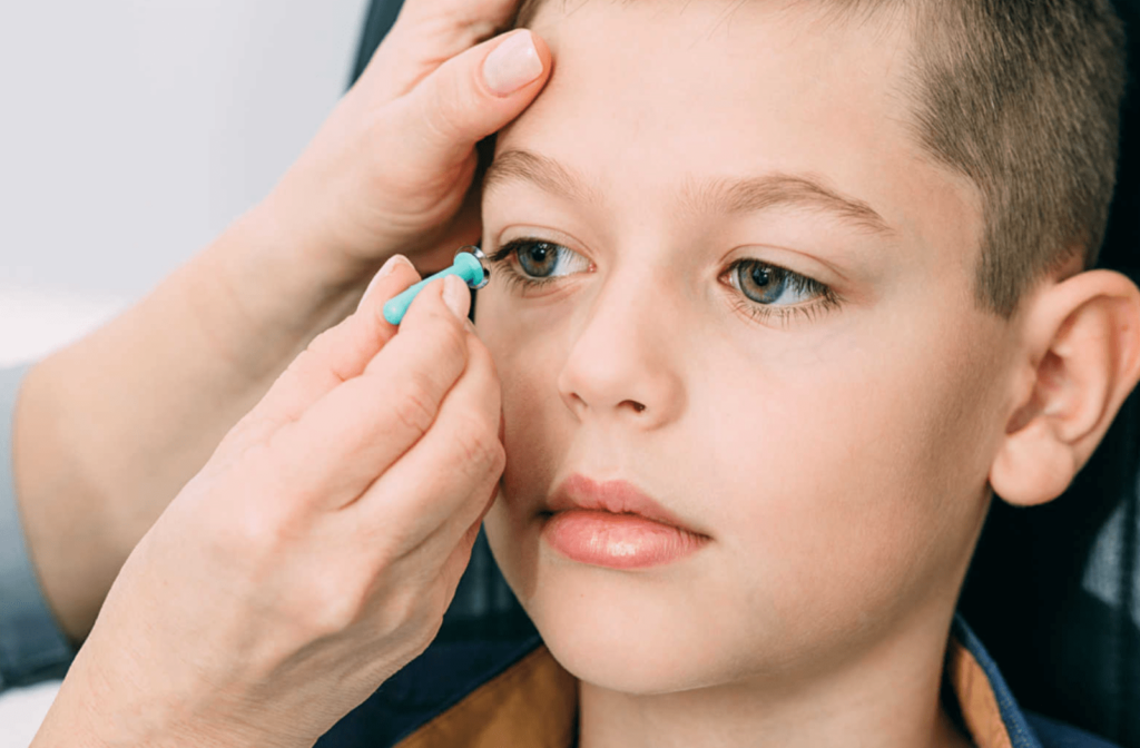 A right hand of female eye doctor is holding a scleral contact lens and about to place the contact lens on the right eye of a boy