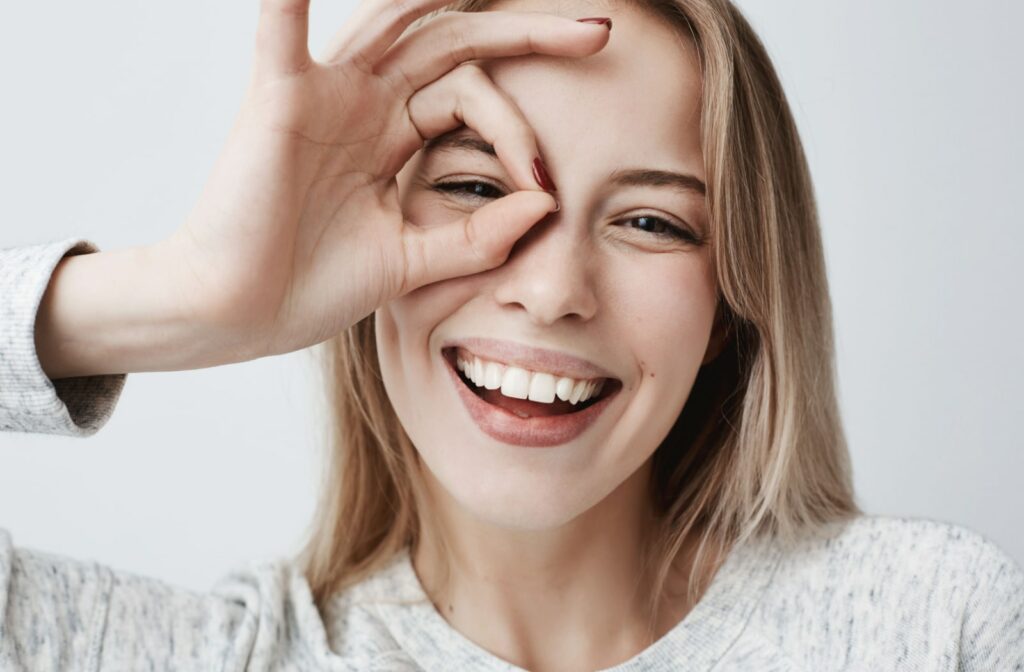 A woman smiling and making a loop with her fingers around her eye.