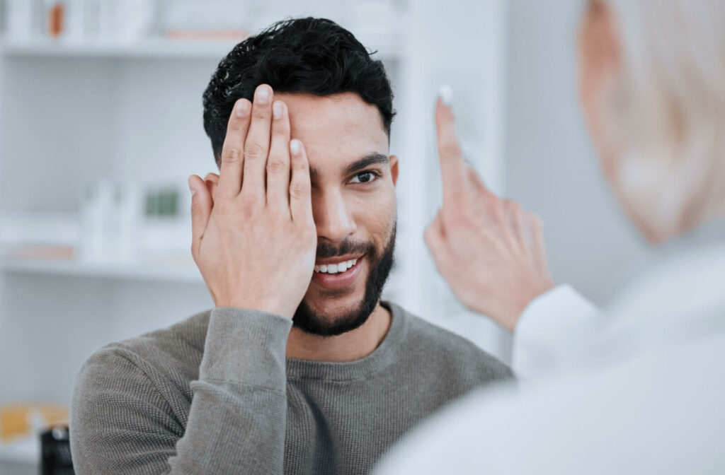 The person is covering one eye during a vision test while following a doctor’s finger in an eye exam room.