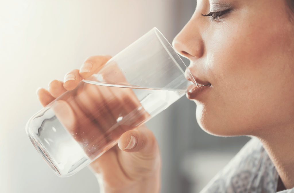 A woman drinks a glass of water to keep her body and eyes hydrated throughout warm months.