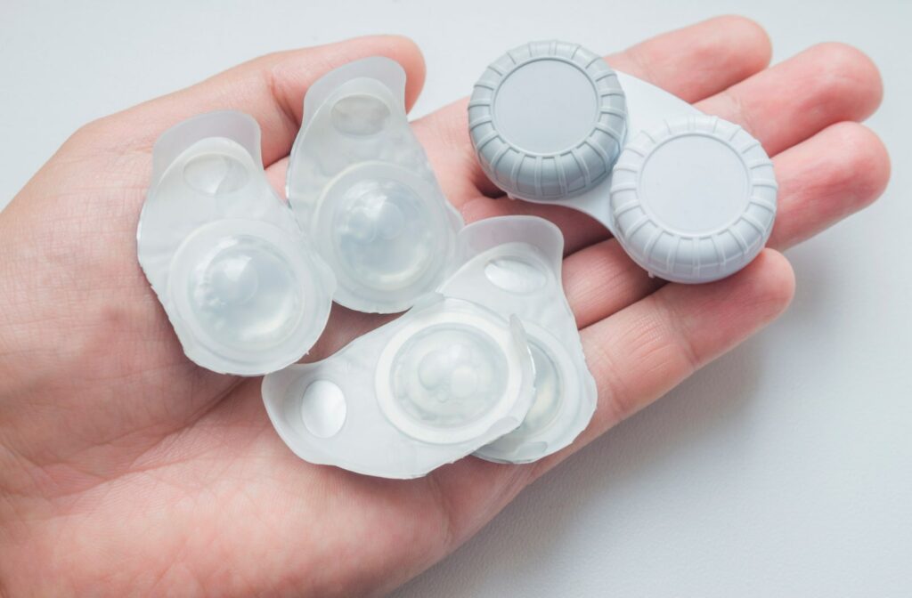 A person holding a few packs of daily contact lenses and a regular contact lens case in their hand.