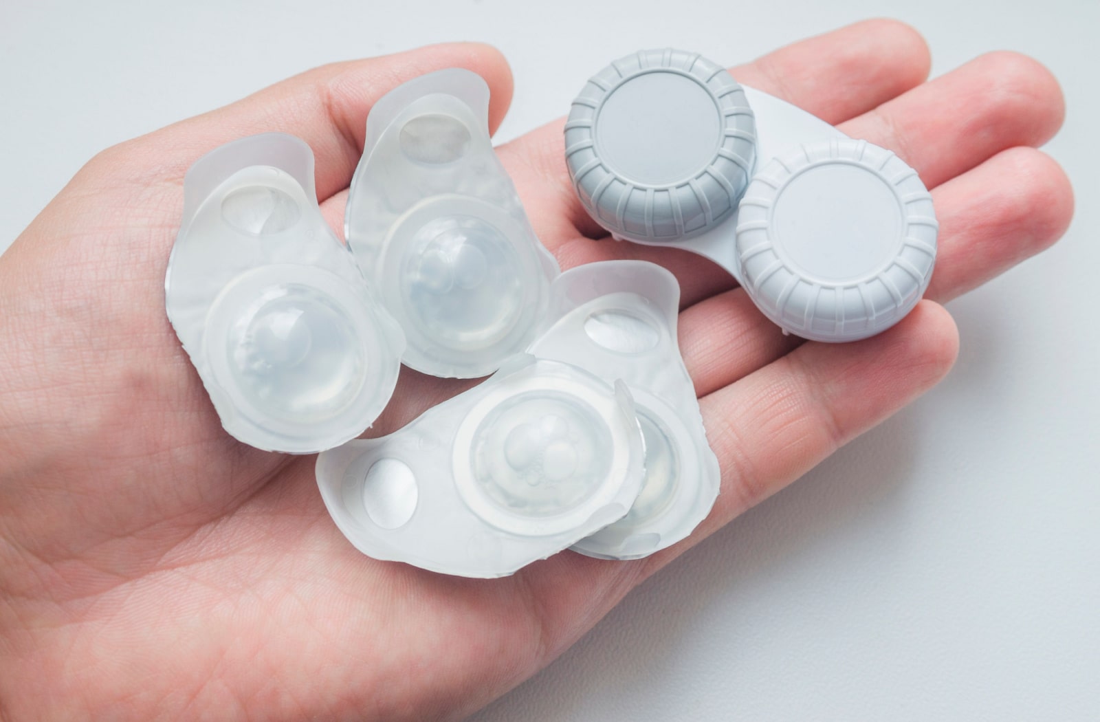 A person holding a few packs of daily contact lenses and a regular contact lens case in their hand.