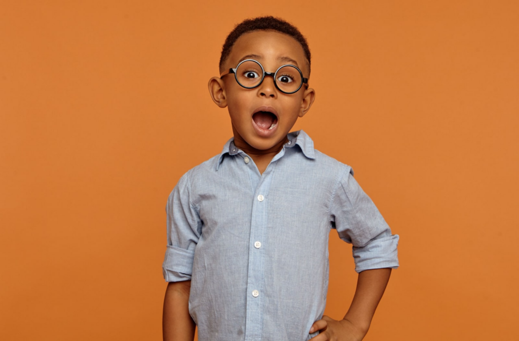A young boy standing in front of a burnt orange background, with his mouth open like he's surprised