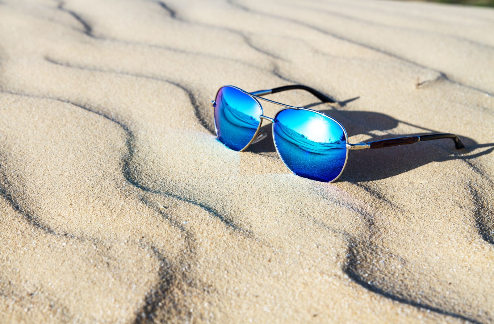 A pair of polarized sunglasses sitting in the sand on a beach.