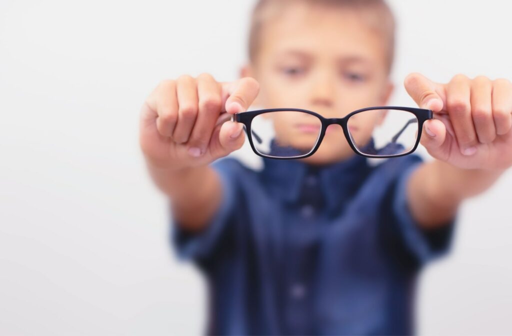 A young boy holding out a pair of vision-correcting glasses. The boy is out of focus while the glasses are in focus. Glasses are a common method to slow the progression of myopia in children.