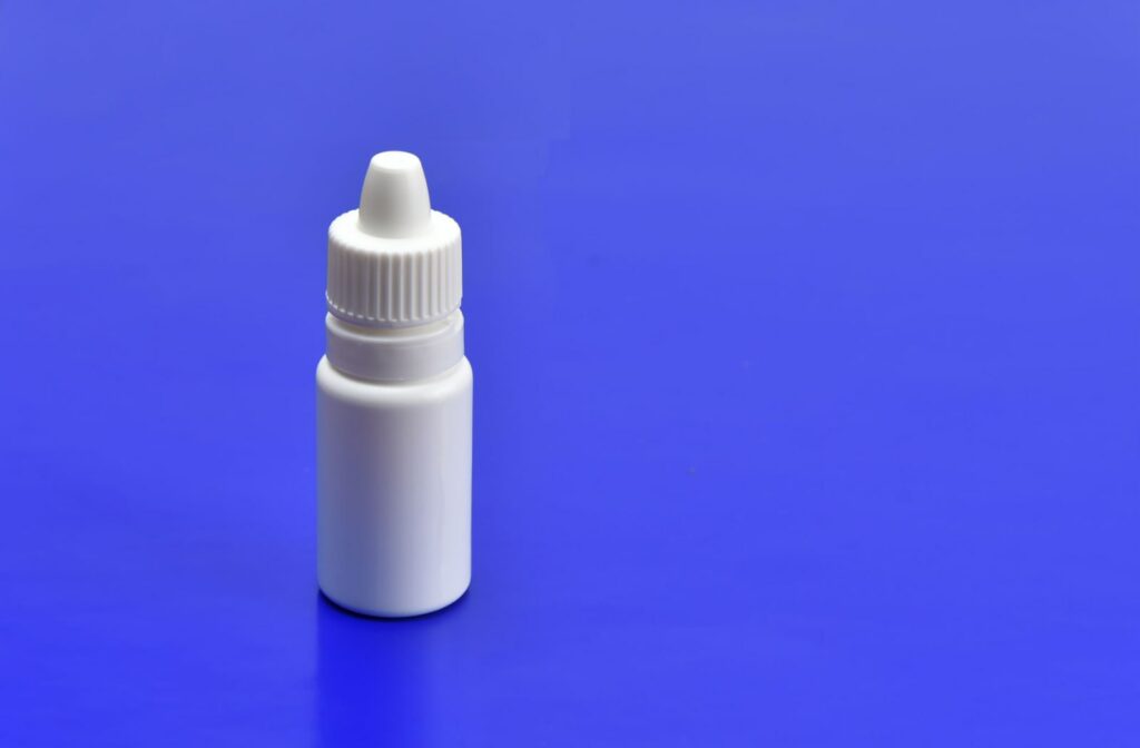 A small, unmarked bottle of eye drops sitting against a blue background