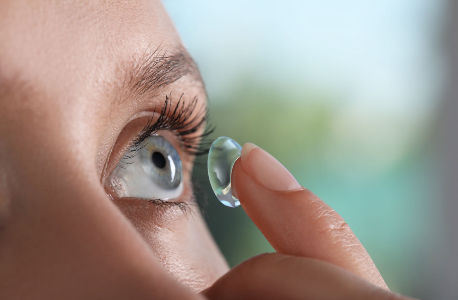 A woman using her index finger to place a contact lens onto her eye