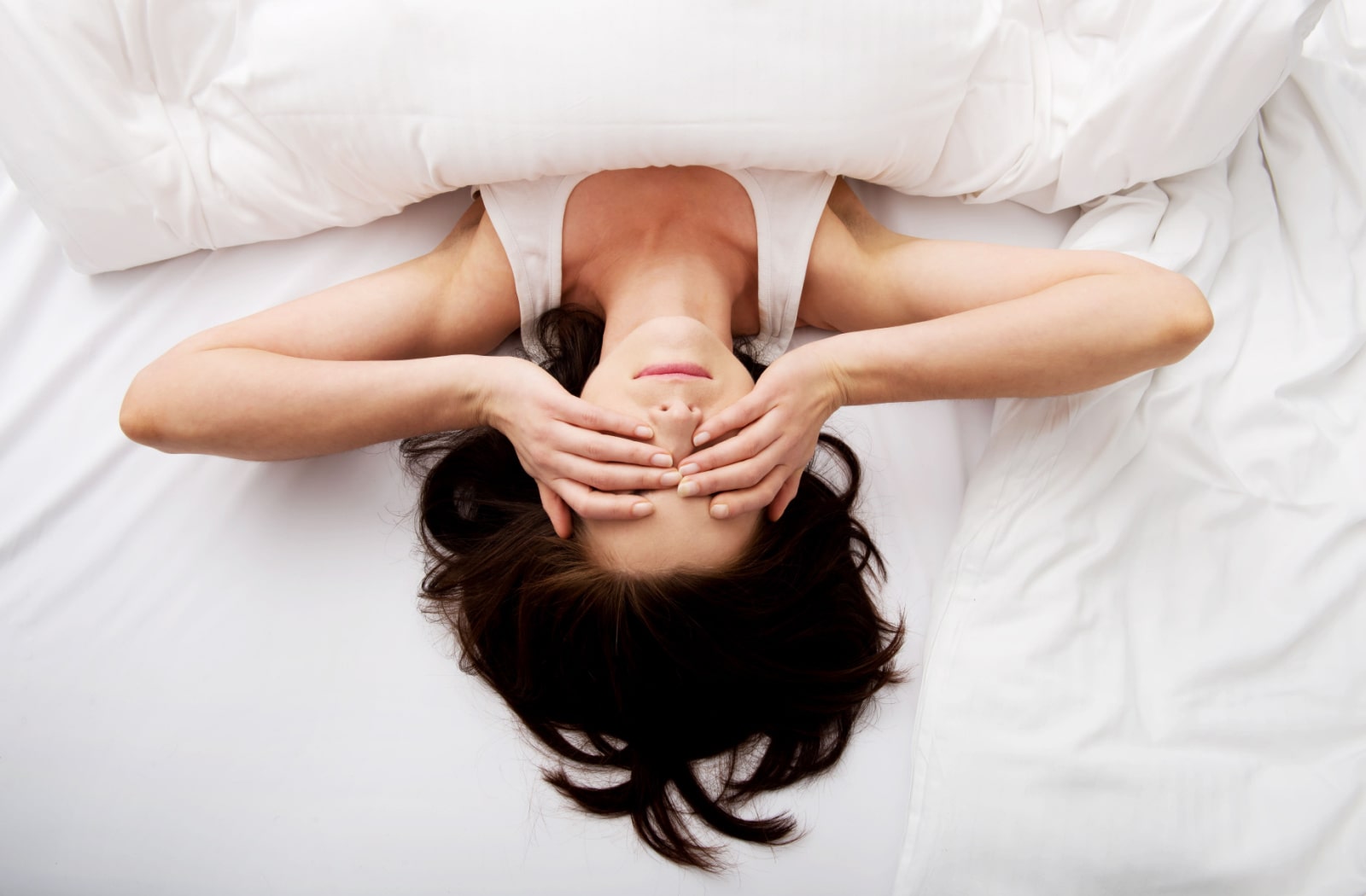 A woman laying in bed with both of her hands over her eyes