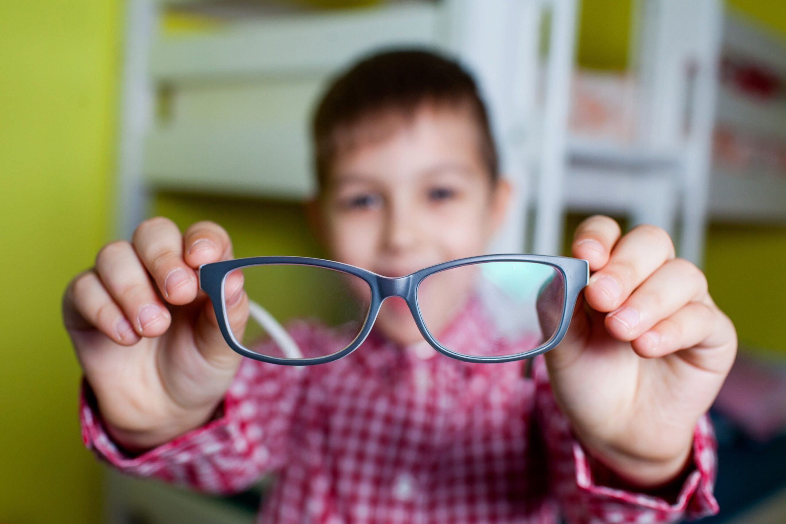 A young boy holding out a pair of glasses in front of him