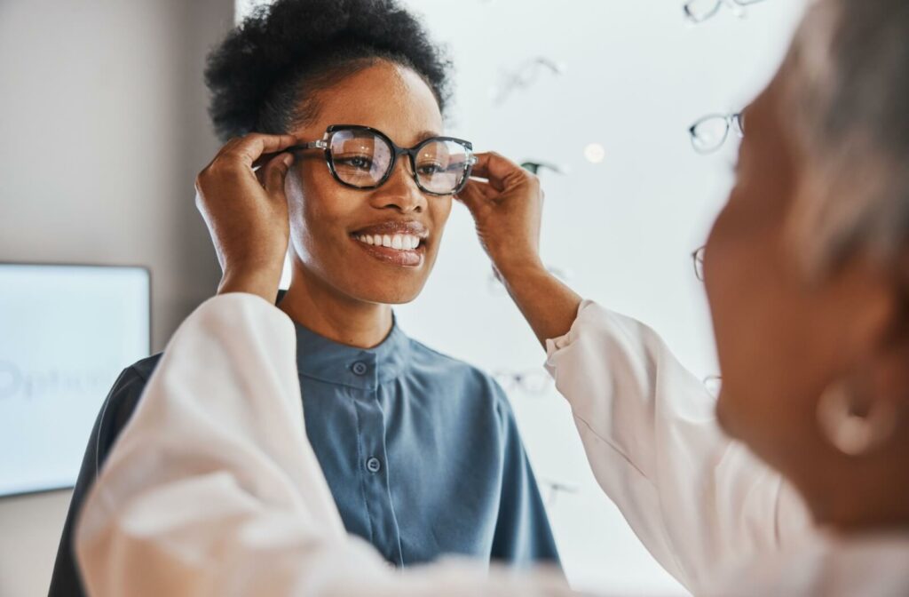 An optometrist puts on glasses on a young woman.