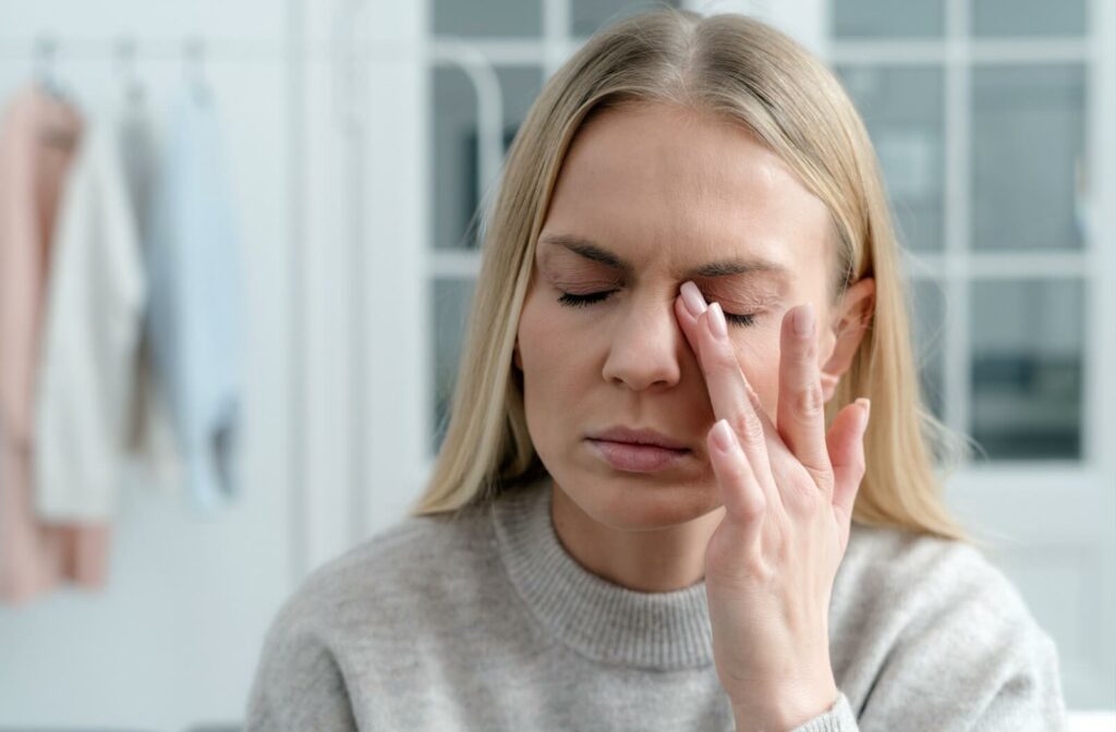 A blonde woman touches her left eye in discomfort, possibly suffering from dry eye and headaches.