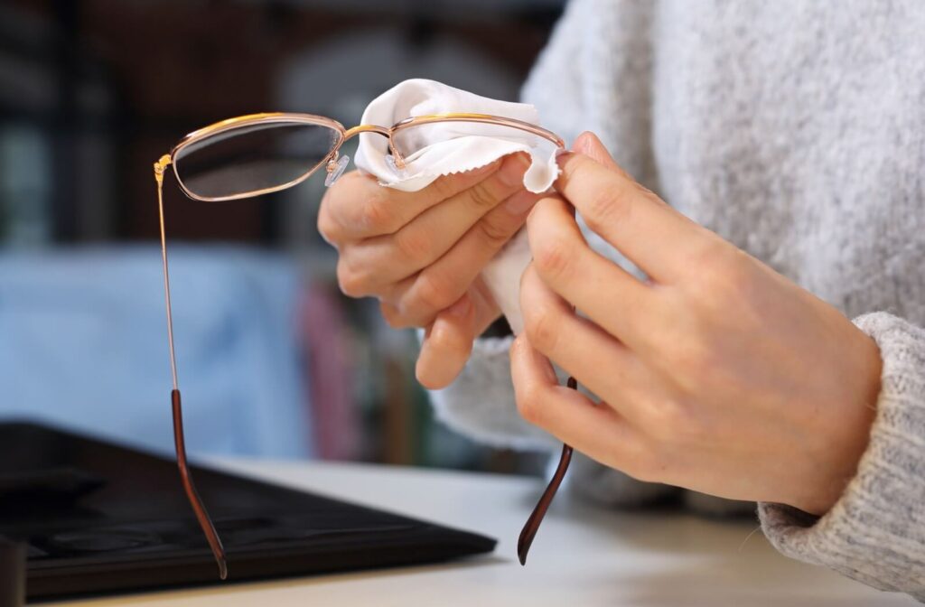 A patient holding glasses in their left hand and using their right hand to wipe them clean with a microfibre cloth to prevent scratches.