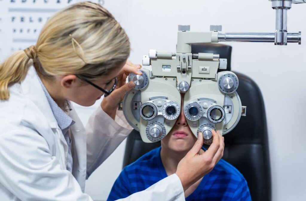 A child sits in the exam chair and looks through a phoroptor during their routine eye exam while their eye doctor adjusts the lens power.