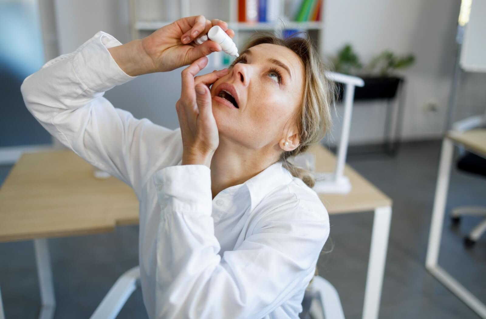 An adult tilts their had back and puts eye drops in their eyes to alleviate dry eye symptoms.