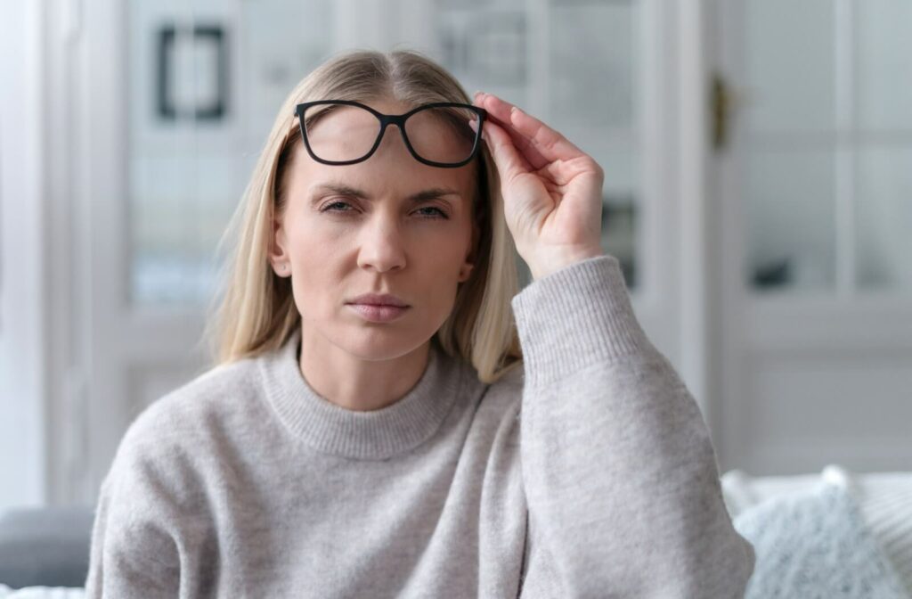 A person lifts their eyeglasses and squints to try and see clearly.