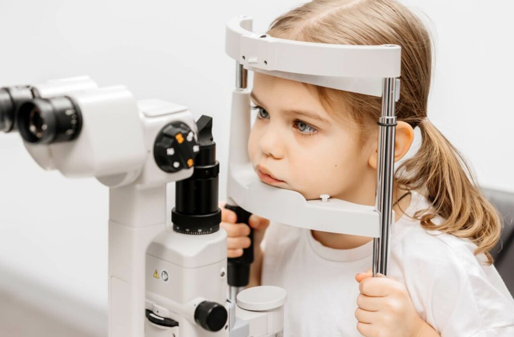 A young child with a focused expression laying their chin and holding onto bars on a slit lamp, which is optometry equipment with a rack for resting one's face.