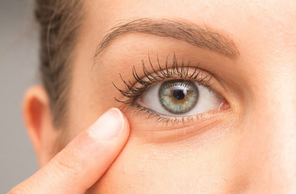 Close-up of a person gently touching the skin below their eye, highlighting the eye’s iris, lashes, and eyelid area.