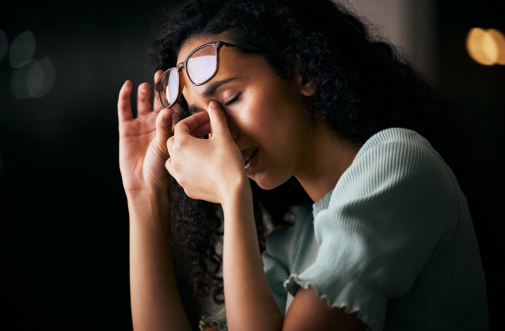Person showing signs of eye strain and possible dizziness, with one hand pressing the forehead while holding glasses.