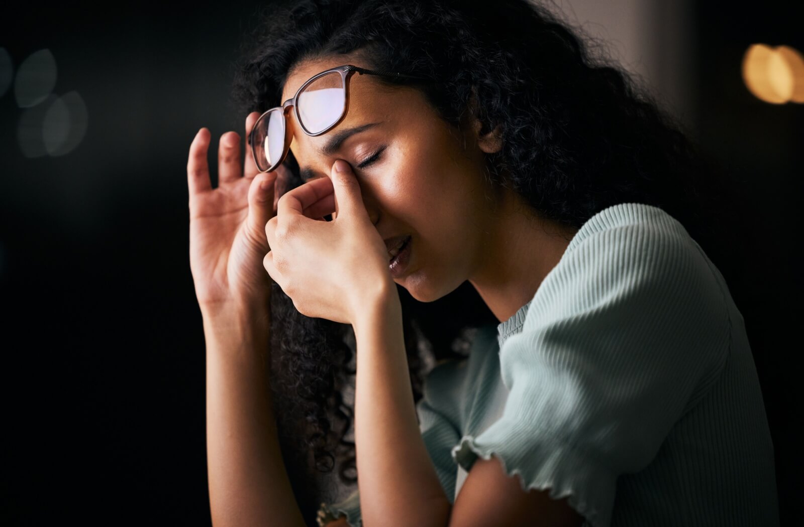 Person showing signs of eye strain and possible dizziness, with one hand pressing the forehead while holding glasses.