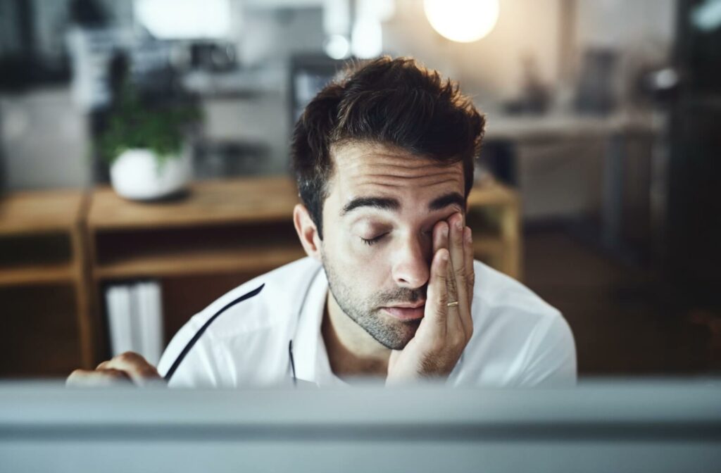 An individual resting their head in their hand and rubbing their tired eyes while working at a computer.